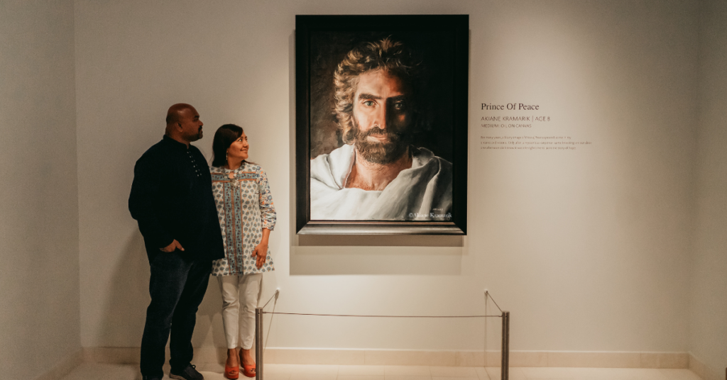 Pradeep and Fabiola standing together in front of Akiane Kramarik’s Prince of Peace painting at Beloved Gallery.