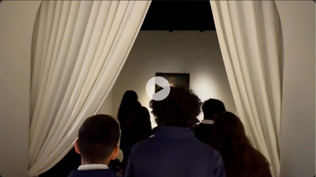 A group of people seen from behind enter a dimly lit room through white curtains, facing a framed artwork on the wall.