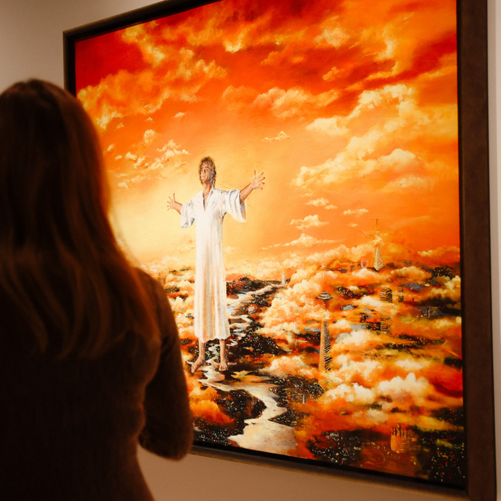 A visitor viewing Akiane Kramarik's painting "Jesus: The Missing Years," depicting a young Jesus in a white robe hovering over a cityscape that blends past, present, and future architectural styles, set against a vibrant orange sunset sky.