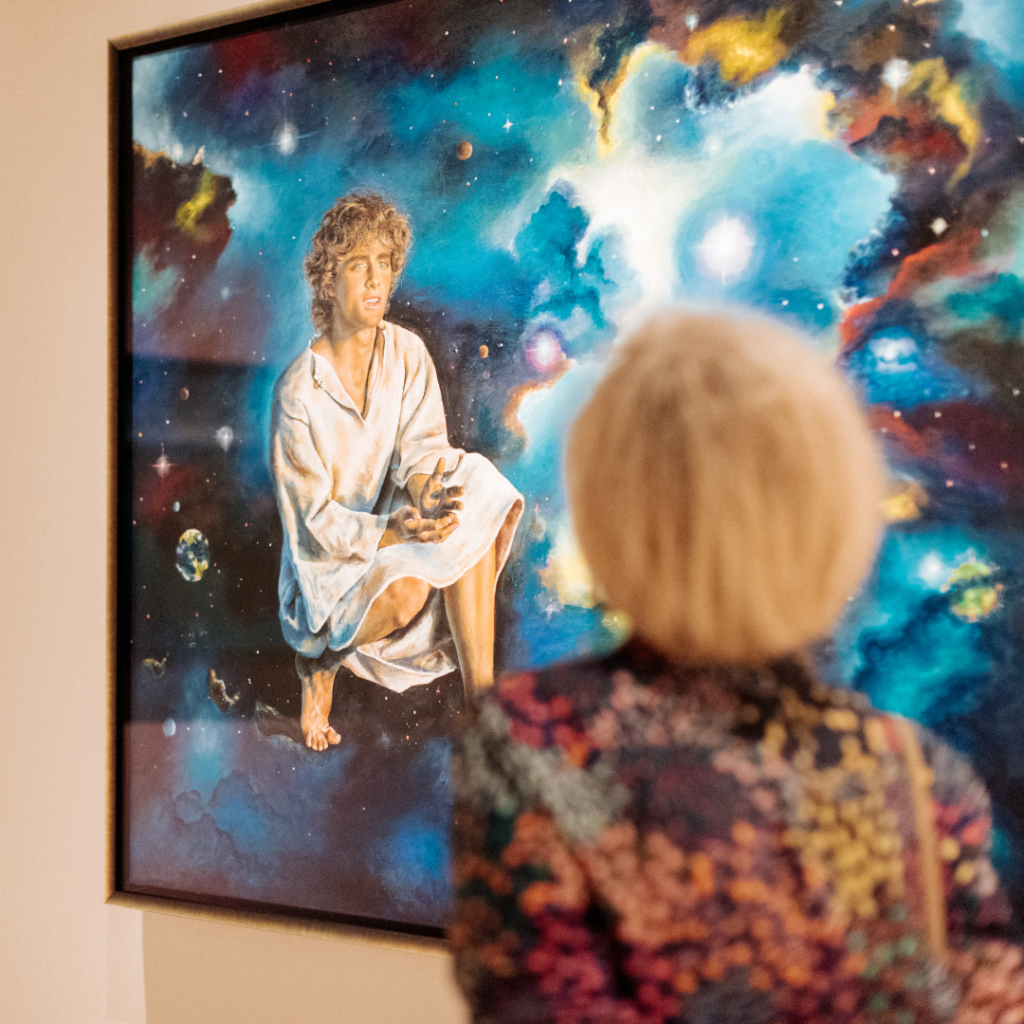 Visitor admiring Akiane Kramarik’s Jesus: The Missing Years painting at Beloved Gallery, surrounded by celestial imagery.