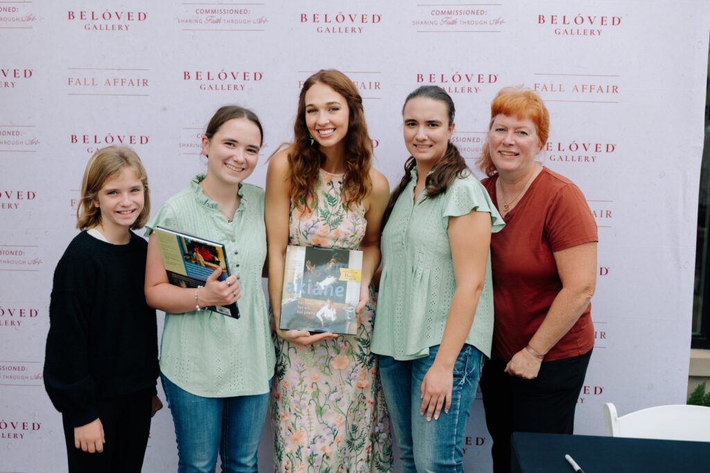 Five people posing in front of a Beloved Gallery backdrop; two girls and three women smiling, two holding magazines.