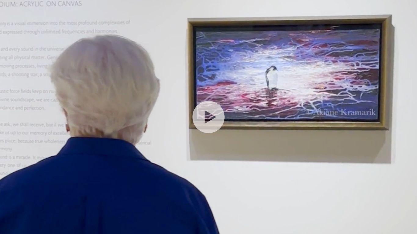 Back of an elderly person with white hair in a blue jacket standing in a gallery, looking at a framed abstract painting on the wall.