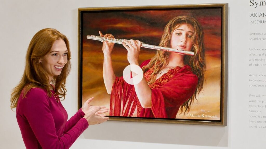 A woman in a magenta top smiles and gestures toward a painting of a woman playing the flute, displayed on a white wall with descriptive text beside it.
