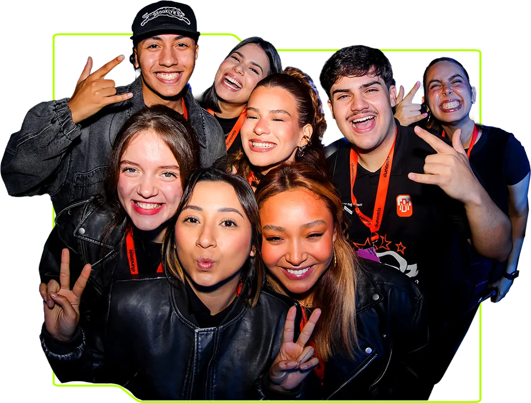 A group of eight young people smile and pose closely together, some making peace signs and rock hand gestures, wearing casual clothes and lanyards.