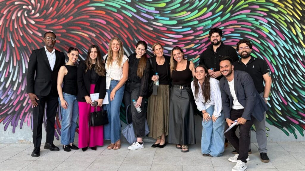 A diverse group of eleven people standing and posing in front of a colorful, swirling mural.